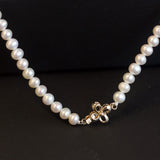 A white freshwater pearl necklace with an 18K gold bow-shaped clasp.