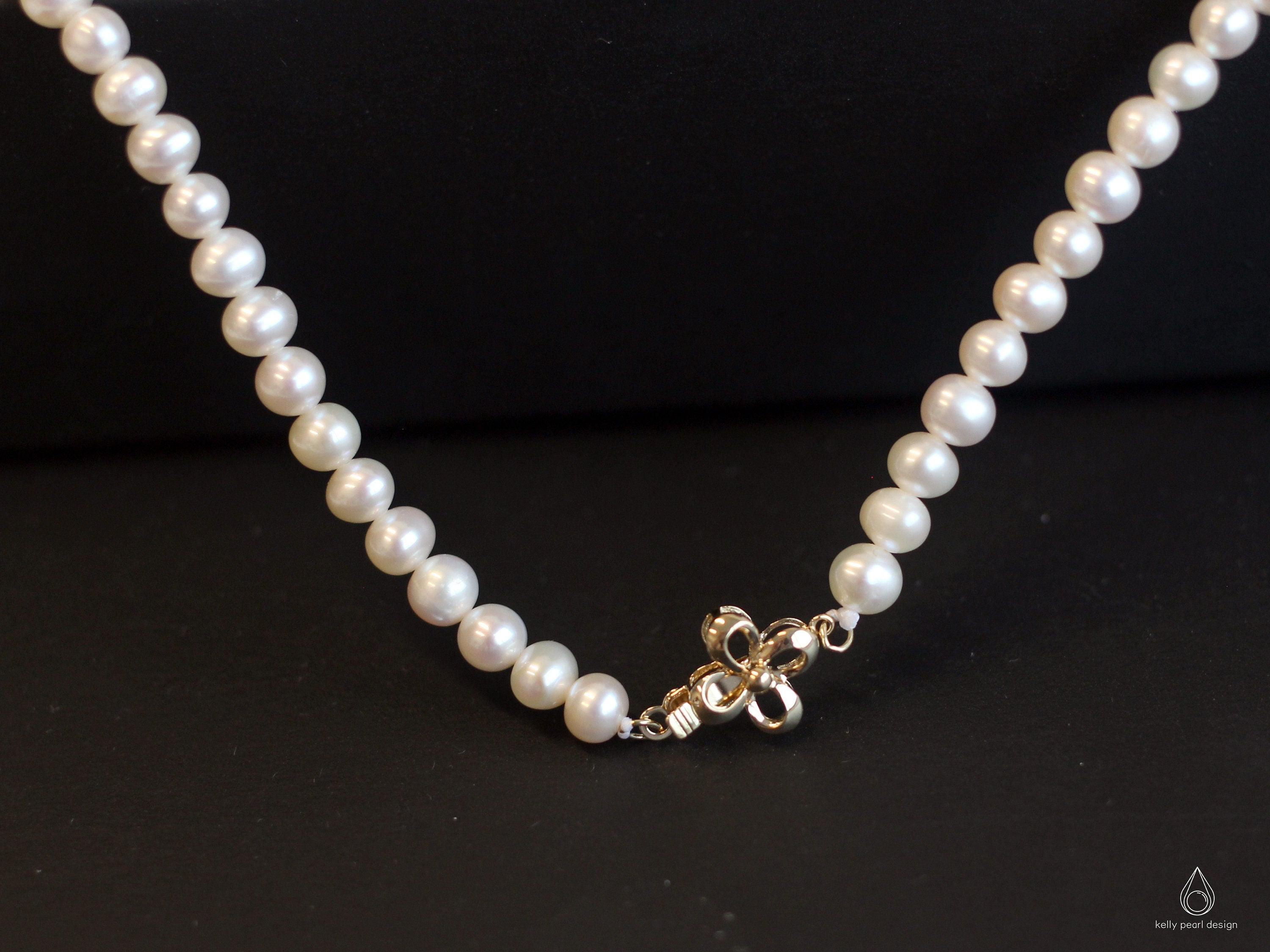 A white freshwater pearl necklace with an 18K gold bow-shaped clasp.