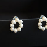 Two flower-shaped stud earrings, each made of small white pearls, are displayed on a black surface.