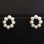 Two flower-shaped stud earrings, each made of seven freshwater pearls, are displayed on a black surface.