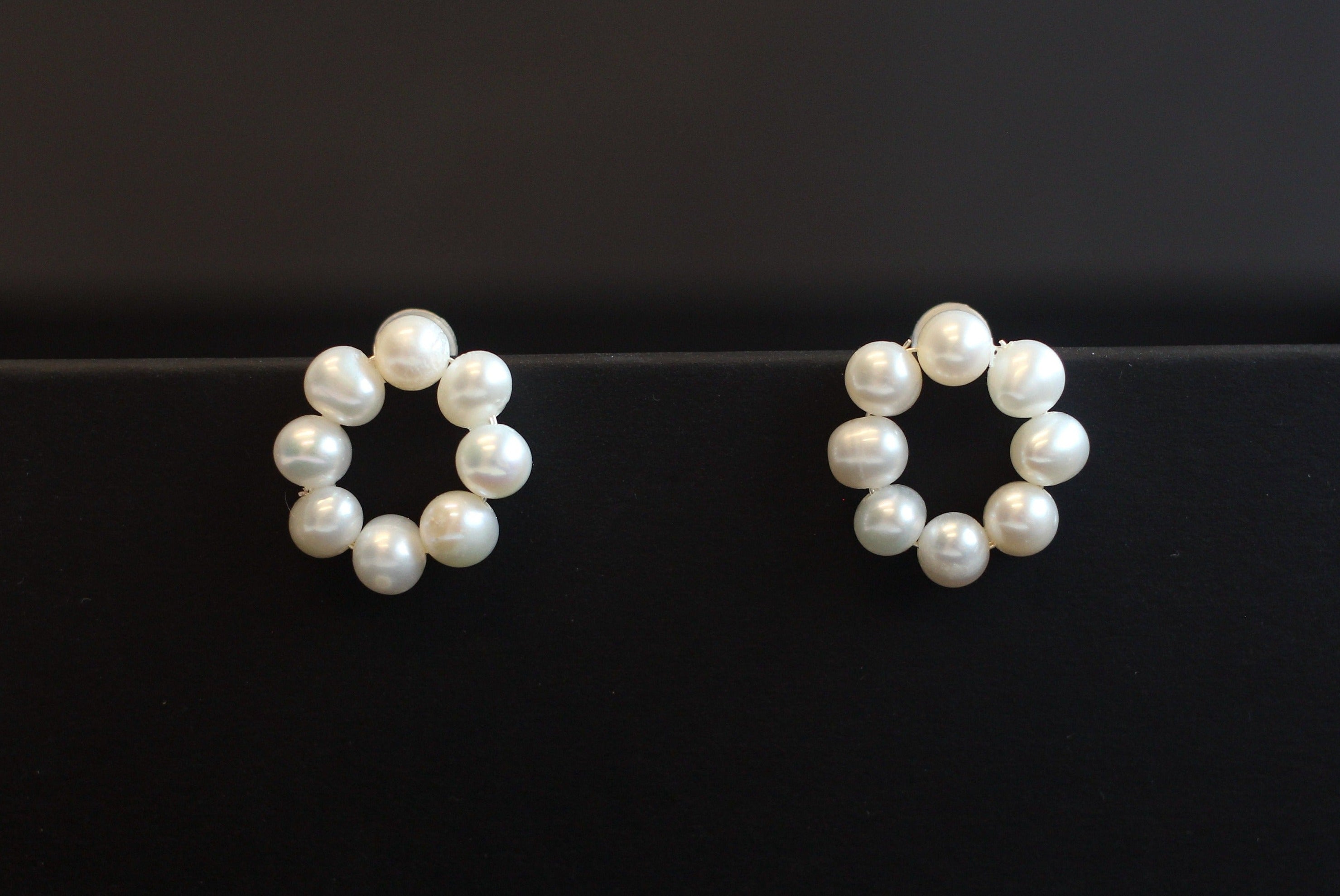 Two flower-shaped stud earrings, each made of seven freshwater pearls, are displayed on a black surface.