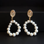 Two gold and freshwater pearl hoop earrings are displayed on a black surface.