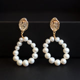 Two gold and freshwater pearl hoop earrings are displayed on a black surface.