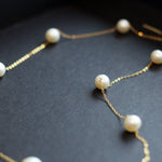 Dainty pearl necklace with a 14K gold-plated chain on a dark background.