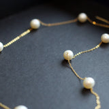 Dainty pearl necklace with a 14K gold-plated chain on a dark background.