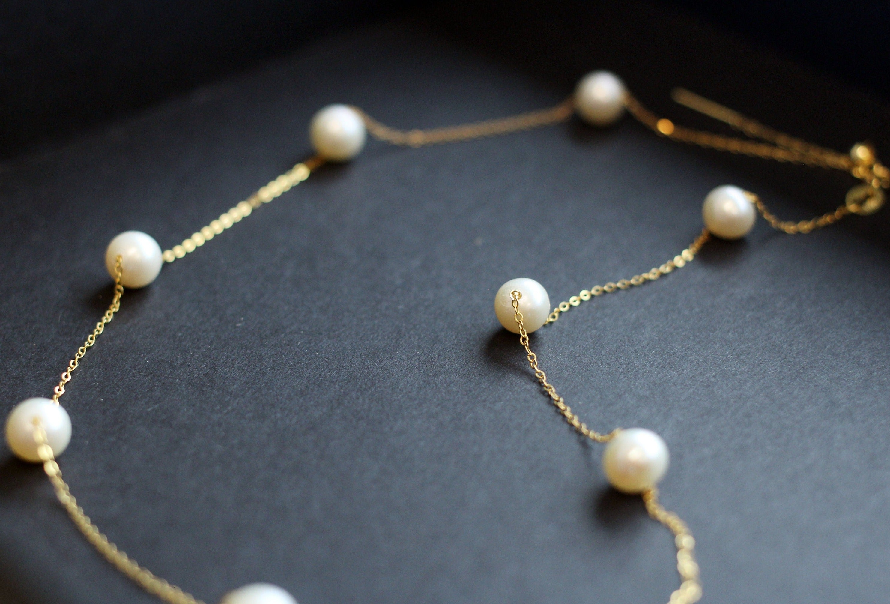 Dainty pearl necklace with a 14K gold-plated chain on a dark background.