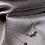 A delicate gold chain necklace featuring three white pearls, displayed on a silver-grey fabric.