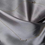 A dainty gold chain necklace features three small pearls and two gold beads.