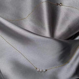 A dainty gold chain necklace features three small pearls and two gold beads.