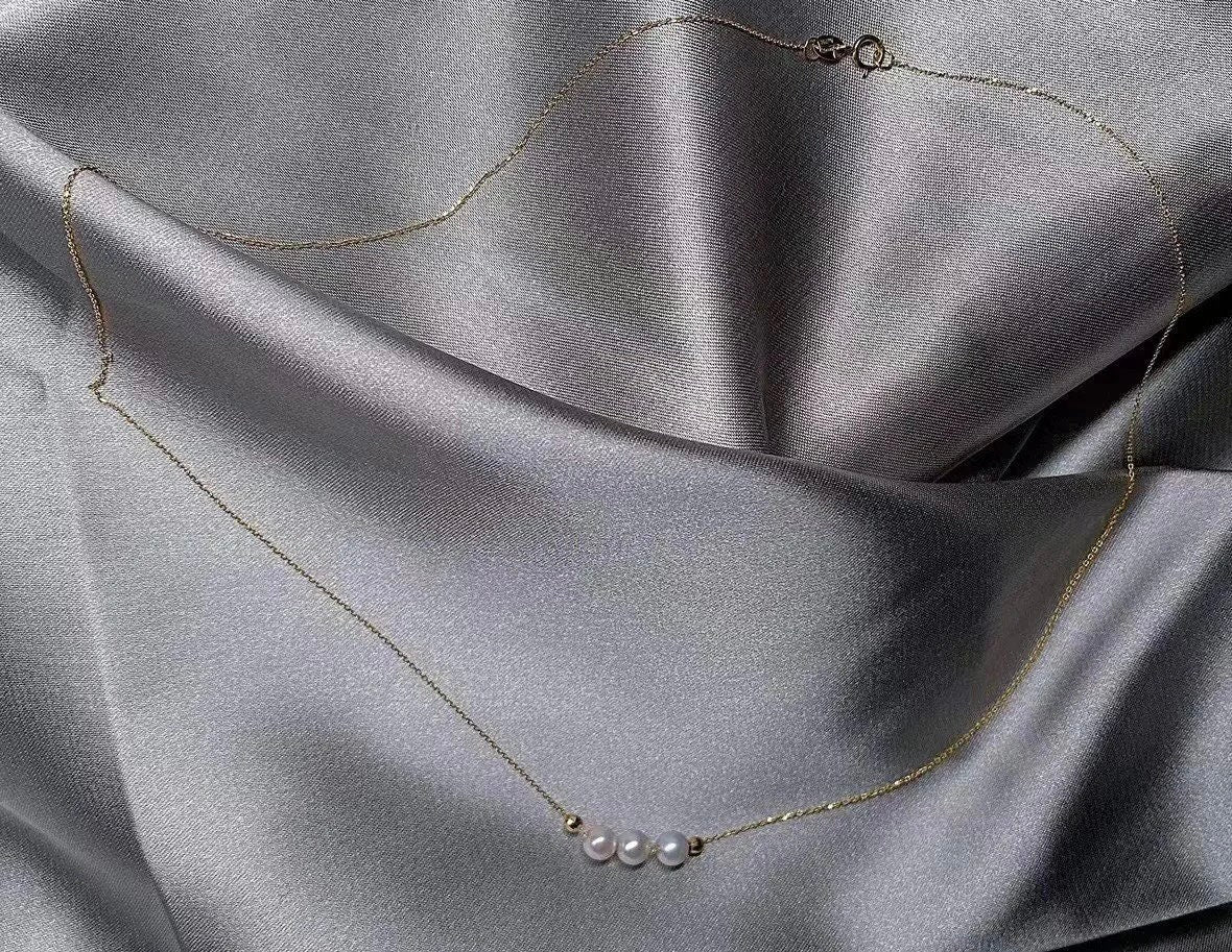 A dainty gold chain necklace features three small pearls and two gold beads.