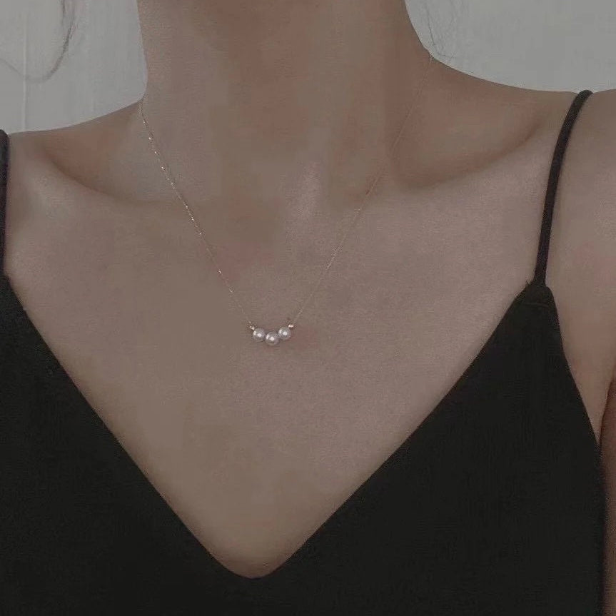 Three pearl bead necklace with a gold-plated chain on a person's neck.