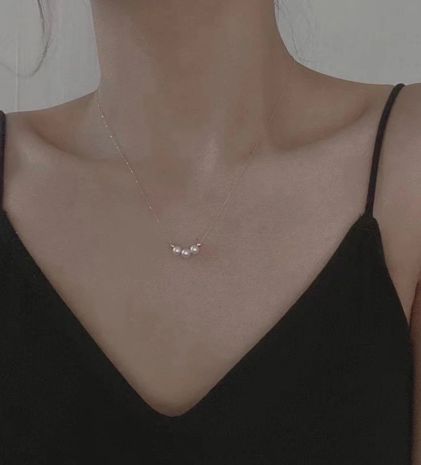 Three pearl bead necklace with a gold-plated chain on a person's neck.