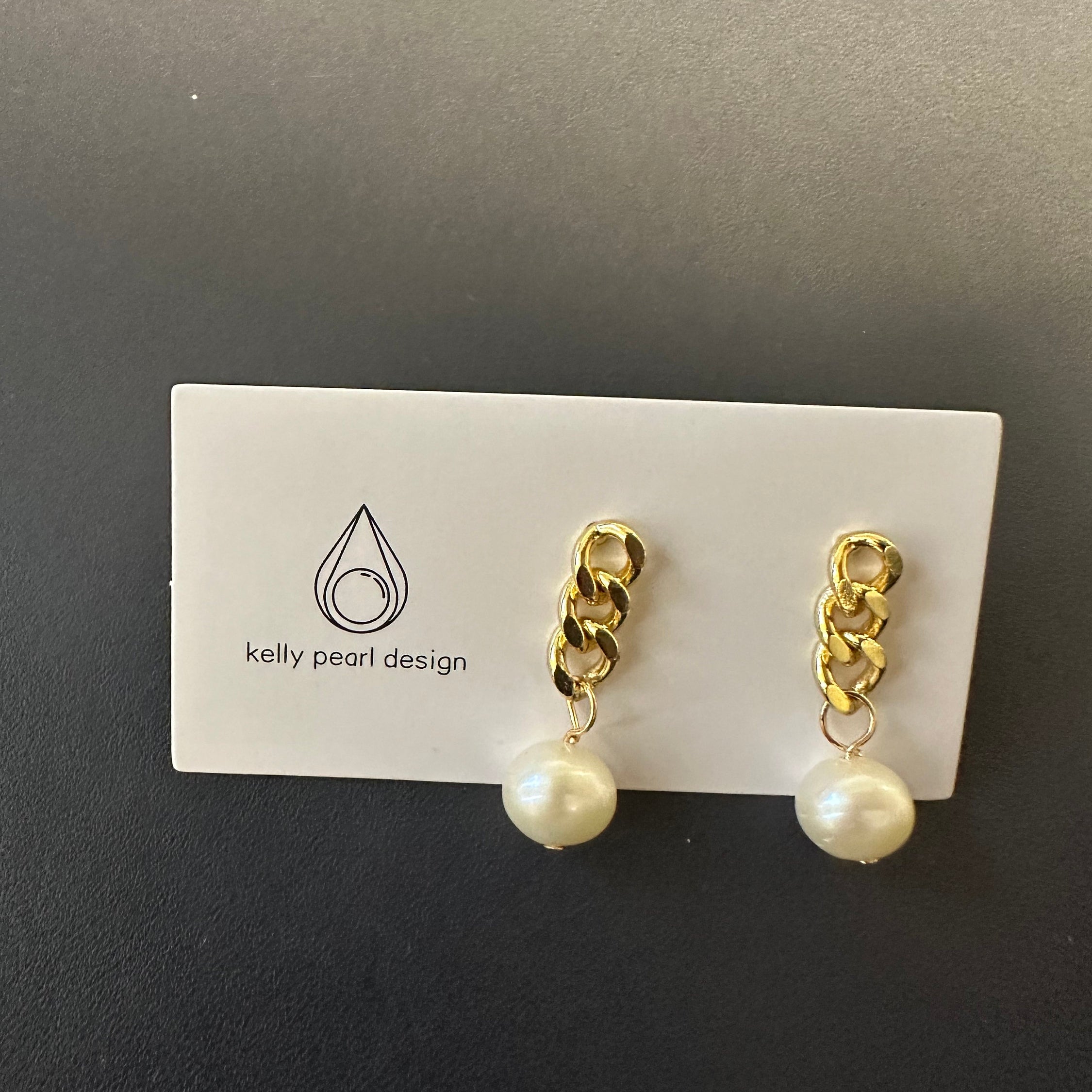 Gold chain earrings with a single white pearl drop on a white card.