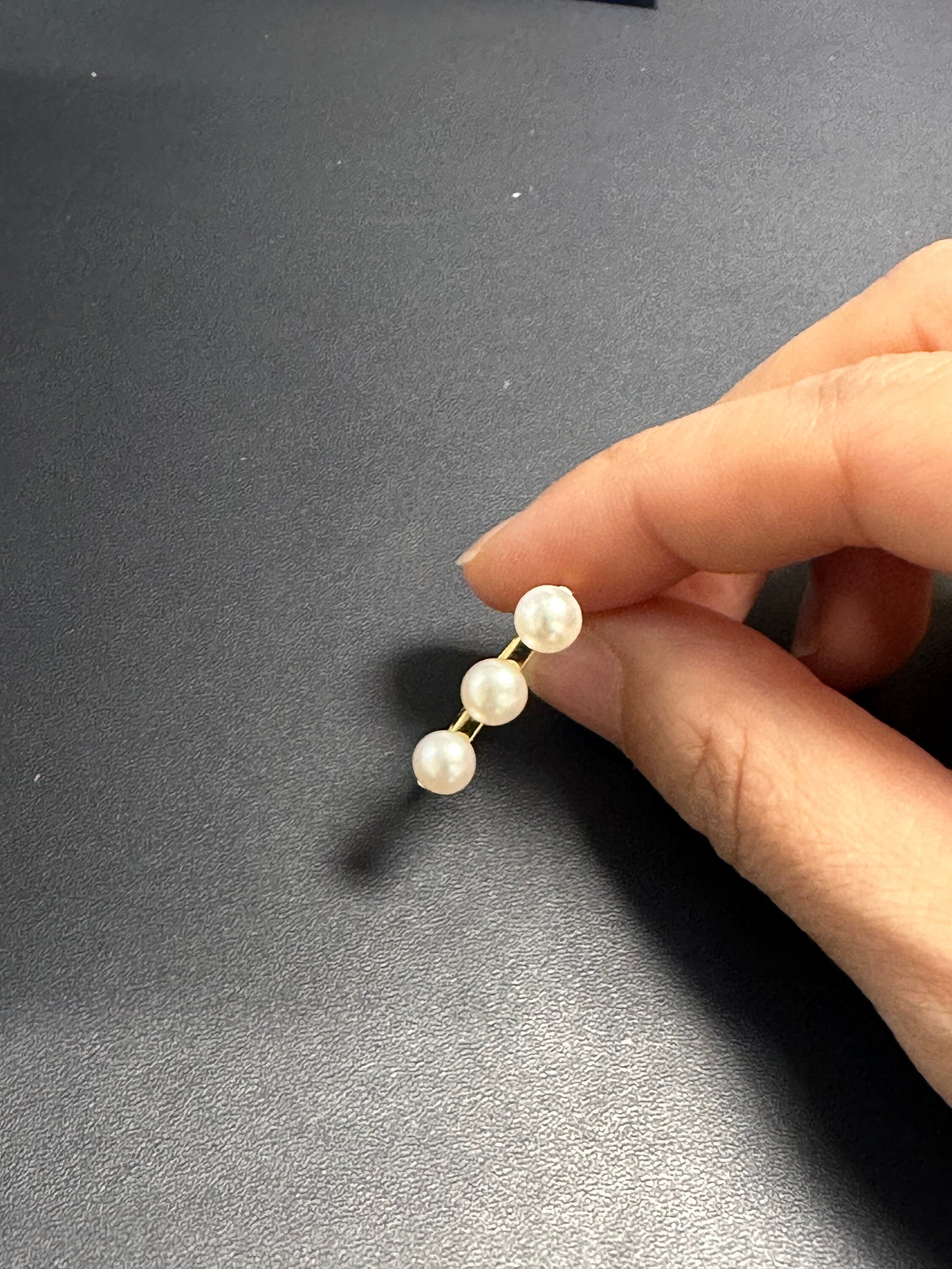 A hand holds a gold ring with three freshwater pearls.