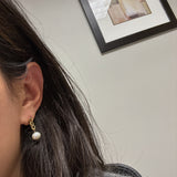 A woman wears a gold chain earring with a white freshwater pearl drop.