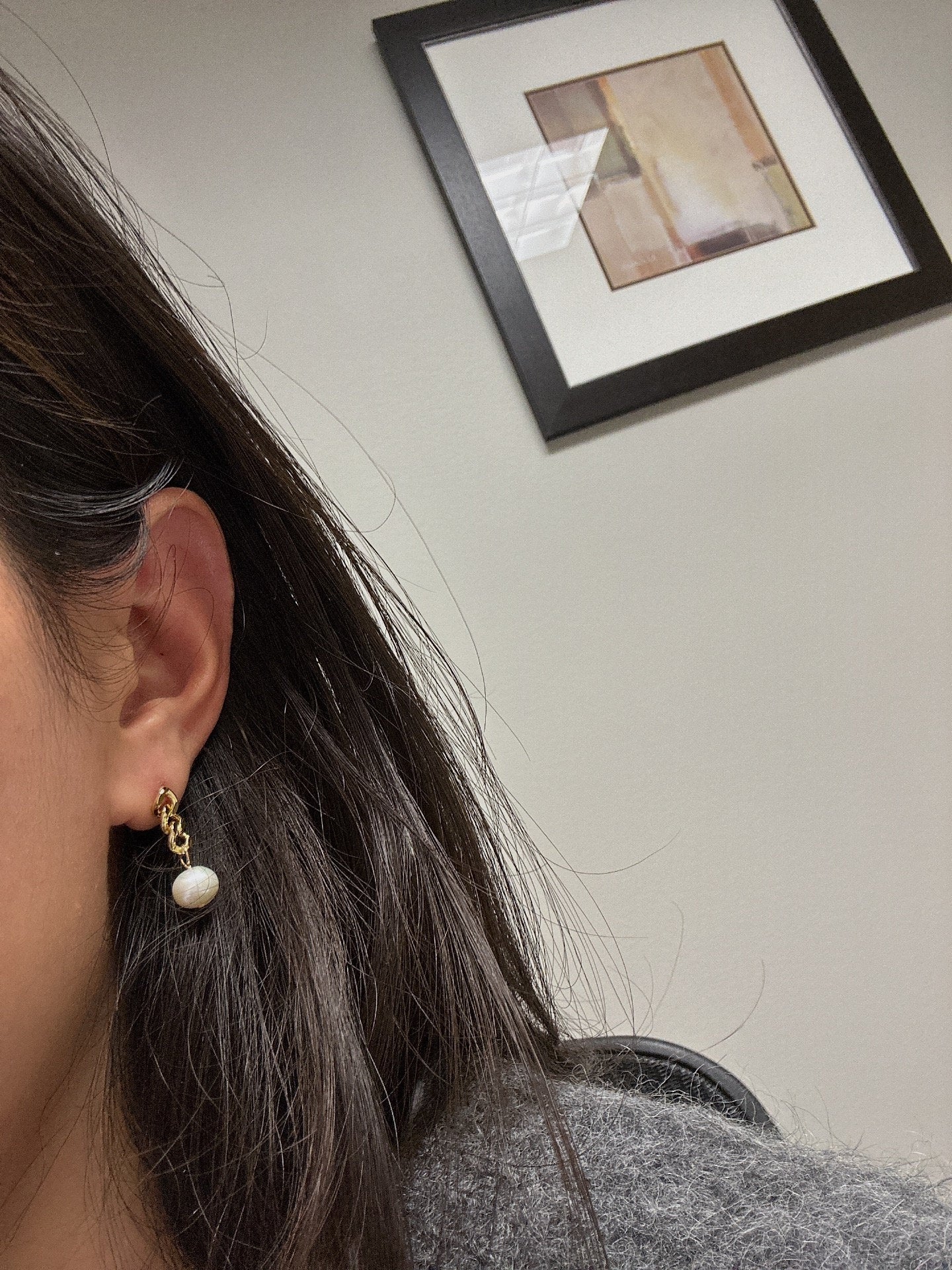A woman wears a gold chain earring with a white freshwater pearl drop.
