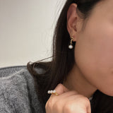 A woman wears a gold chain earring with a single freshwater pearl drop and a pearl ring.