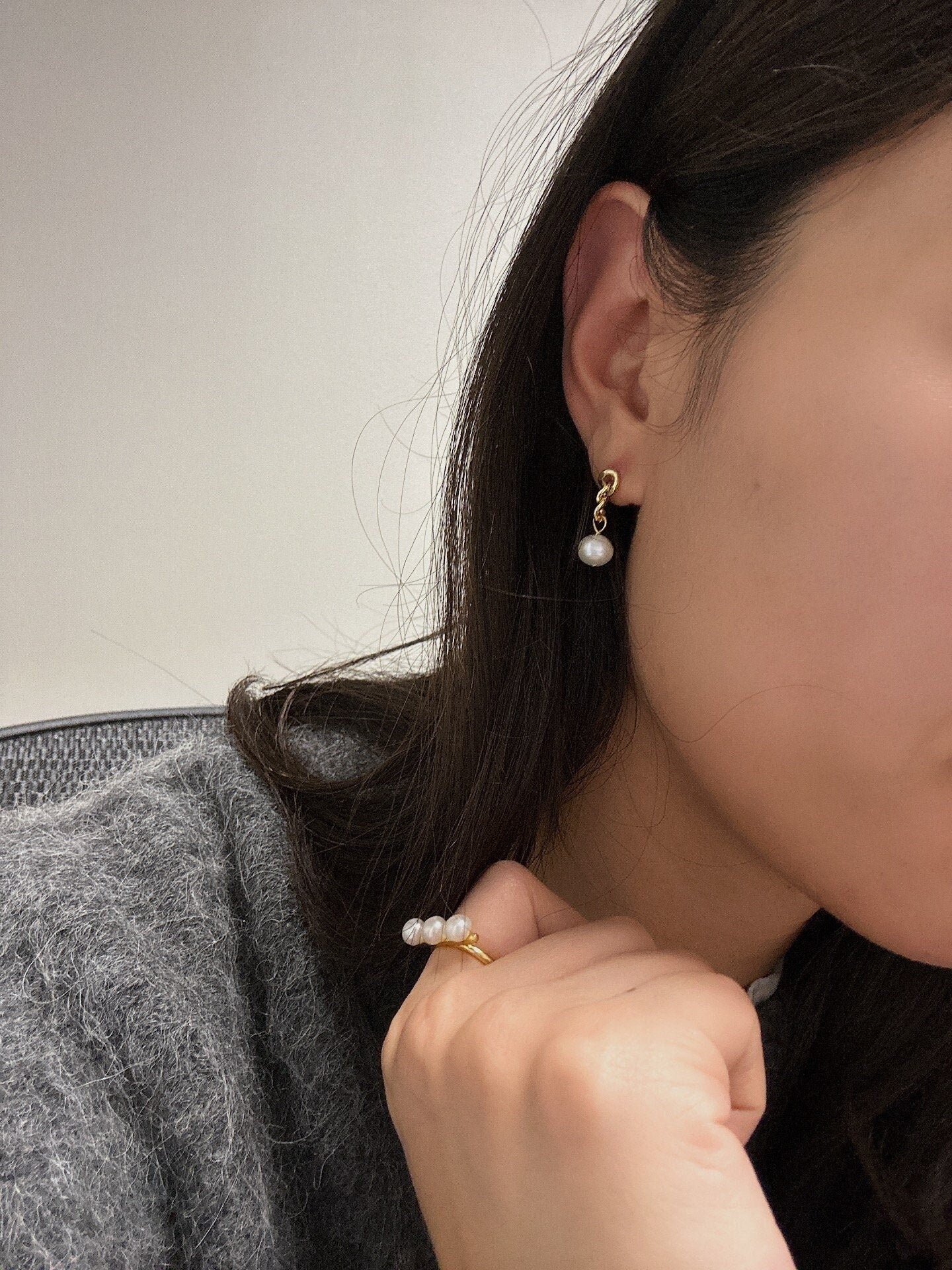 A woman wears a gold chain earring with a single freshwater pearl drop and a pearl ring.