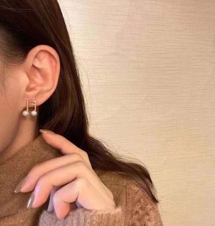 Freshwater pearl musical note stud earrings on a person's ear.