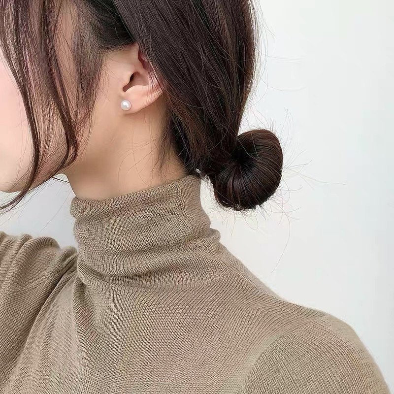 A woman wears a single pearl stud earring and a tan turtleneck sweater.